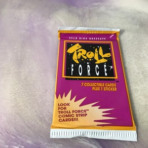 May include: A purple and yellow card pack with the text "Troll Force" and "7 collectible cards plus 1 sticker". The pack also says "Look for Troll Force™ Comic Strip Cards!!!"