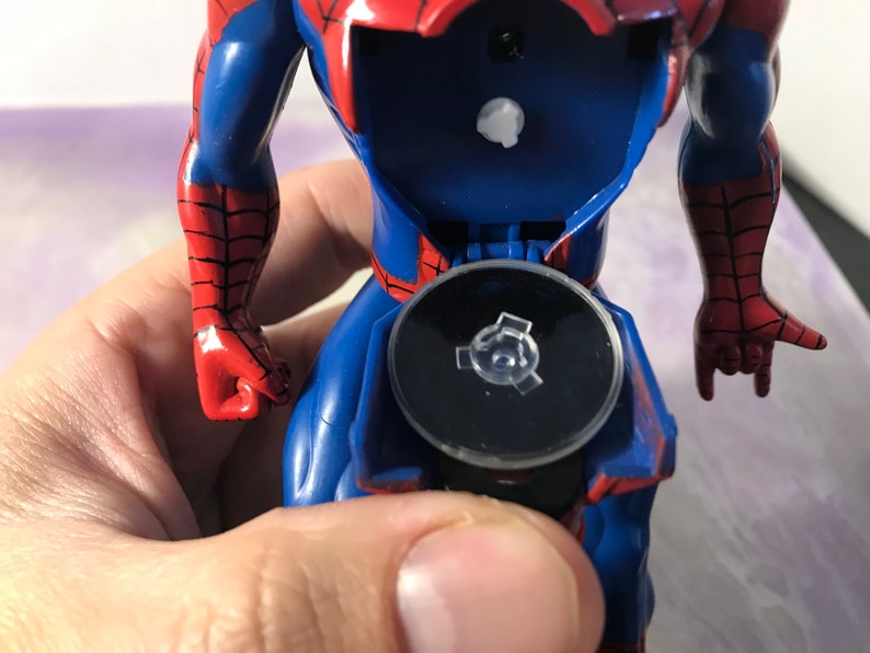 May include: A red and blue plastic action figure of Spider-Man with a black base. The figure is posed with one arm raised and the other arm bent at the elbow. The figure is missing a small piece from the base.