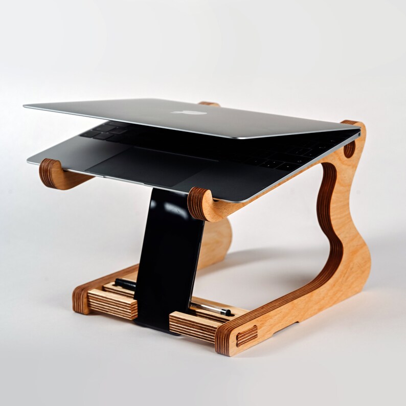 May include: A wooden laptop stand with a natural finish. The stand has a raised platform for a laptop and a lower shelf for a tablet or other items. The stand is designed to elevate the laptop to a more ergonomic viewing height.