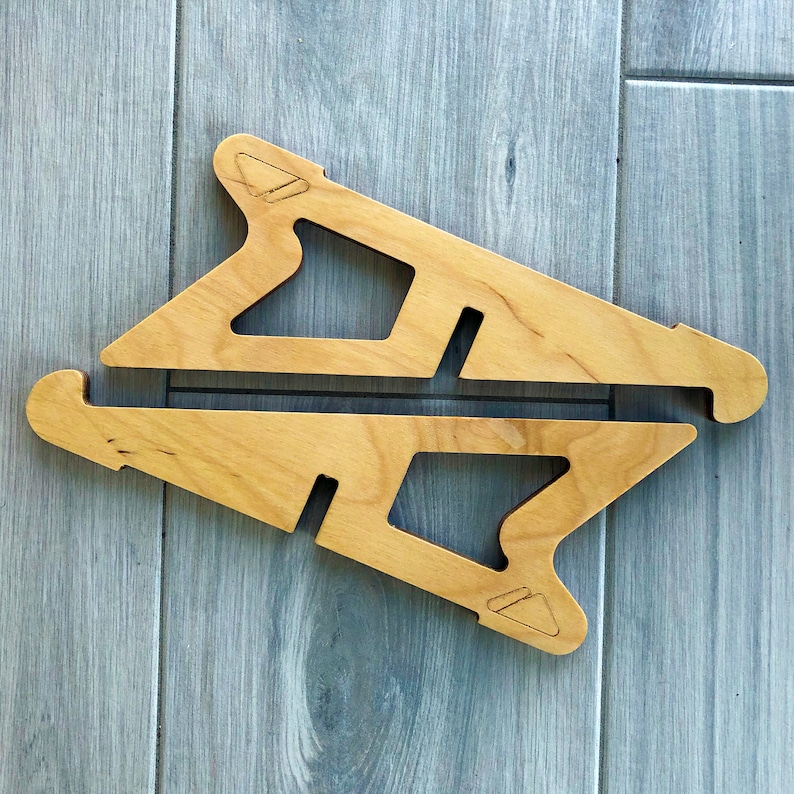 May include: Two light-colored wooden laptop stands. Each stand has a unique cutout design with a triangular notch at the top and a rectangular slot. The stands are designed to elevate a laptop for improved ergonomics.