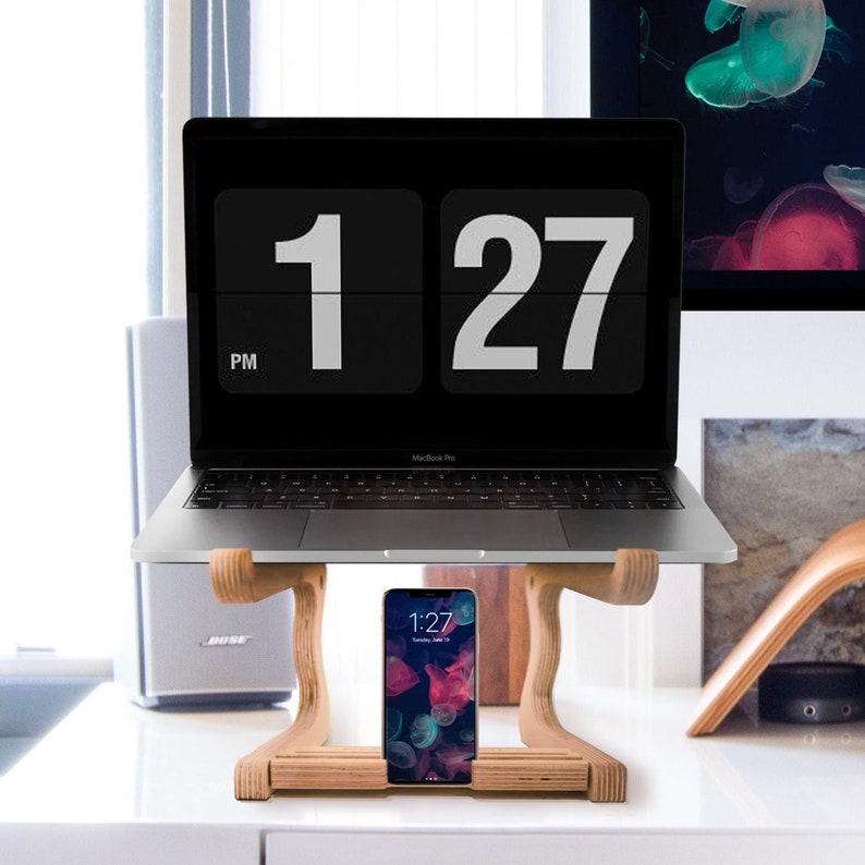 May include: A wooden laptop stand with a laptop on top and a smartphone on the bottom shelf. The laptop screen shows a digital clock displaying 1:27 PM.