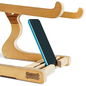 May include: A wooden phone stand with a blue phone resting in the stand. The stand is made of light wood and has a unique design.