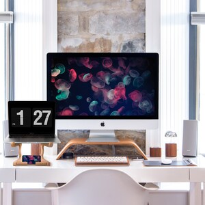 May include: A white desk with a laptop, a desktop computer, a keyboard, a phone, and a vase with flowers. The desktop computer has a screen saver of colorful jellyfish.