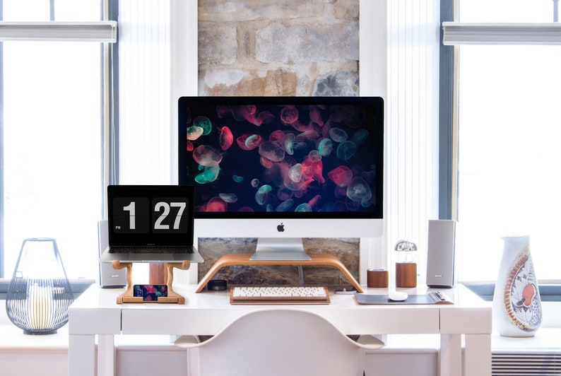 May include: A white desk with a laptop, a desktop computer, a keyboard, a phone, and a vase with flowers. The desktop computer has a screen saver of colorful jellyfish.