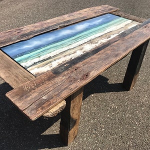 May include: A rustic wooden table with a rectangular glass top featuring a seascape image. The table has two legs made of reclaimed wood.