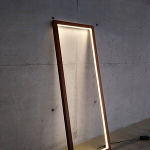May include: A tall, rectangular, wooden frame with a bright white light illuminating the inside. The frame is standing on a gray concrete floor.
