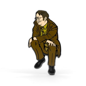 Puede incluir: Un pin de esmalte marrón de un personaje de dibujos animados que lleva un traje marrón y una corbata amarilla, sentado con las piernas cruzadas.