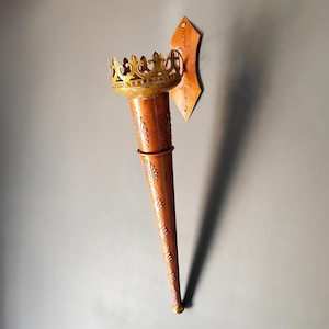 May include: A copper-coloured wall-mounted torch with a crown-shaped top. The torch features ornate leaf patterns and a gold-coloured crown. It is attached to a wooden plaque, ideal for adding a touch of regal decor.