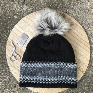 Puede incluir: Un gorro de punto negro con un pomp&oacute;n blanco y un borde con estampado gris y negro.