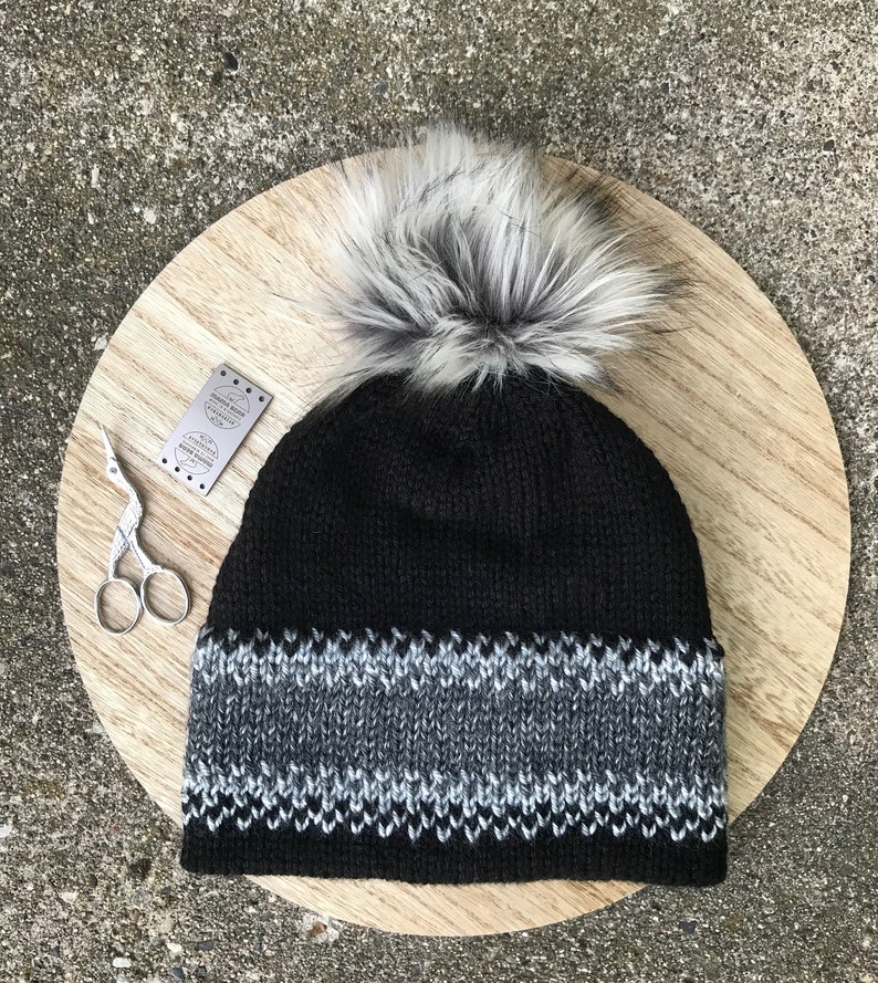 Puede incluir: Un gorro de punto negro con un pomp&oacute;n blanco y un borde con estampado gris y negro.