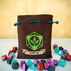 Può includere: Una borsa di velluto marrone con coulisse con un logo di pianta verde e il testo "half-elf" stampato su di essa. La borsa è circondata da dadi colorati con numeri e simboli diversi.
