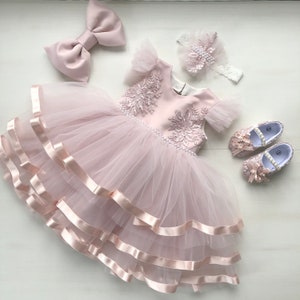 Zartrosa Kleid mit Spitze, Perlen und Schleife. Kleid mit Stirnband und Stiefeln für Babymädchen. Kleid zum ersten Geburtstag.