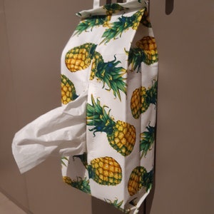 May include: A white tissue box cover with a pineapple print. The cover has a slot for pulling out tissues and hangs from a hook.