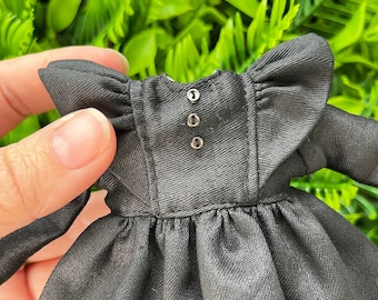 May include: A black dress with a ruffled neckline and long sleeves. The dress has three buttons on the back.