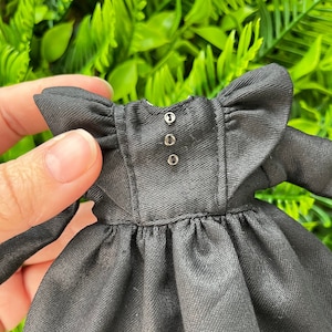 Può includere: Un abito nero con scollo a volant e maniche lunghe. L'abito ha tre bottoni sul retro.