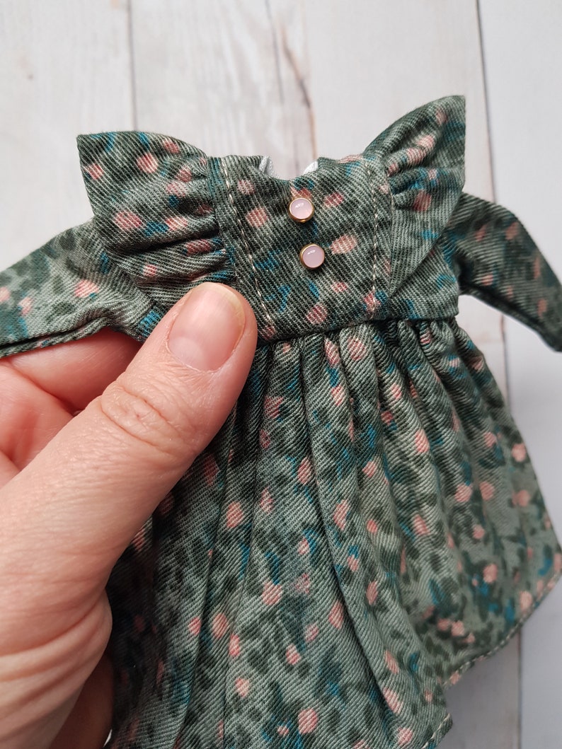 May include: A green and pink floral print dress with a ruffled collar and two gold buttons. The dress is made of a soft, lightweight fabric.