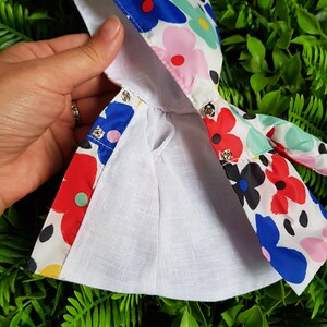 May include: A white hooded raincoat with a colorful floral print featuring red, blue, pink, yellow, and green flowers. The raincoat has a white lining and a drawstring closure.