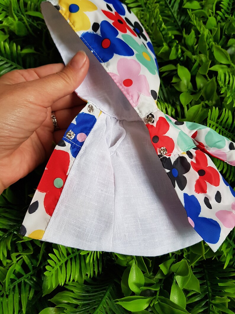 May include: A white hooded raincoat with a colorful floral print featuring red, blue, pink, yellow, and green flowers. The raincoat has a white lining and a drawstring closure.