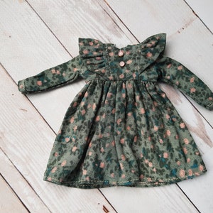 Può includere: Un vestito in velluto a coste verde con stampa floreale rosa e maniche a balze. Il vestito ha una vita arricciata e una chiusura con bottone sul retro.