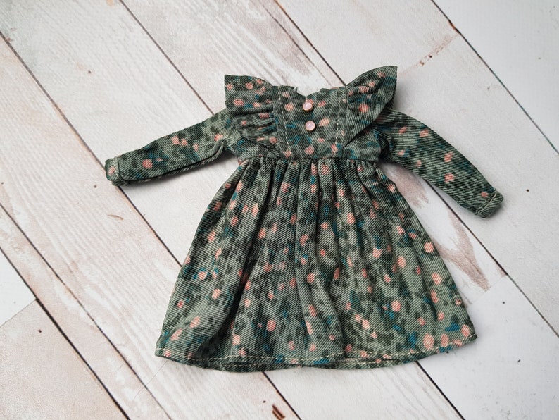 May include: A green corduroy dress with a pink floral print and ruffled sleeves. The dress has a gathered waist and a button closure at the back.