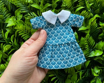 May include: A blue and white patterned dress with a white collar and short sleeves. The dress has a ruffled hem.