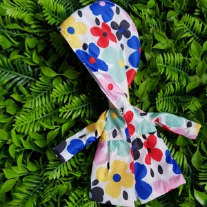 May include: A white raincoat with a hood, featuring a colorful floral pattern with blue, red, yellow, and green flowers. The raincoat is made of a lightweight fabric and has a relaxed fit.