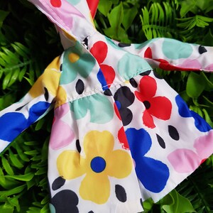 May include: A white hooded jacket with a colorful floral print. The print features red, blue, yellow, pink, and green flowers on a white background.