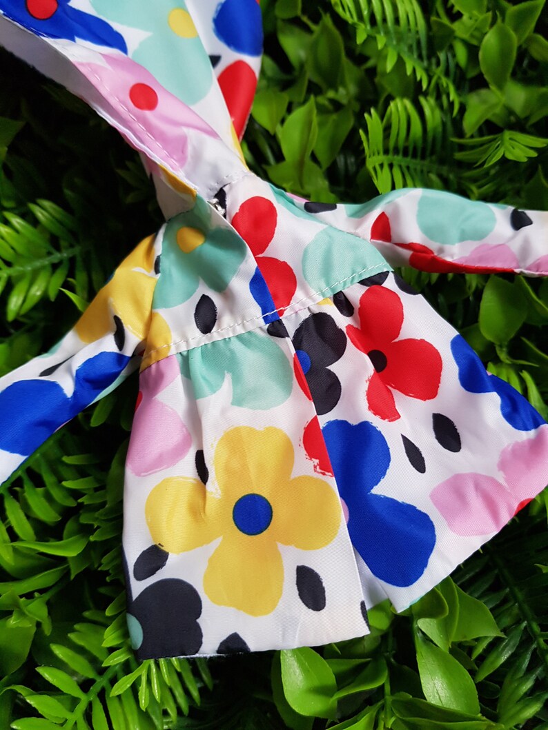 May include: A white hooded jacket with a colorful floral print. The print features red, blue, yellow, pink, and green flowers on a white background.