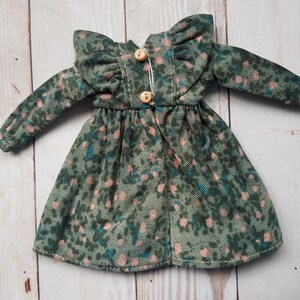 May include: A green and pink floral print dress with long sleeves and a ruffled collar. The dress has a button closure in the back.