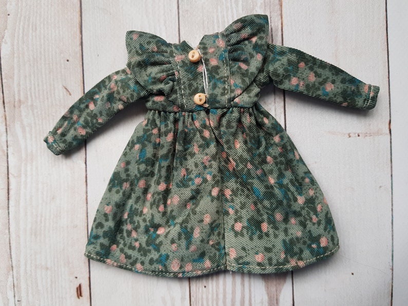 May include: A green and pink floral print dress with long sleeves and a ruffled collar. The dress has a button closure in the back.