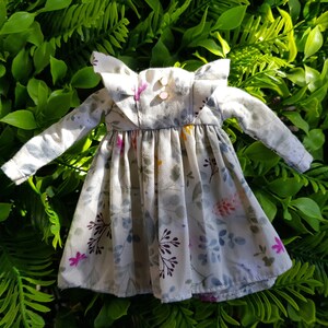 May include: A white dress with a floral print and ruffled collar. The dress has long sleeves and a gathered skirt.
