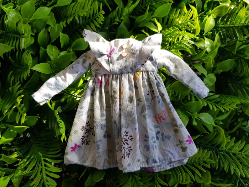 May include: A white dress with a floral print and ruffled collar. The dress has long sleeves and a gathered skirt.