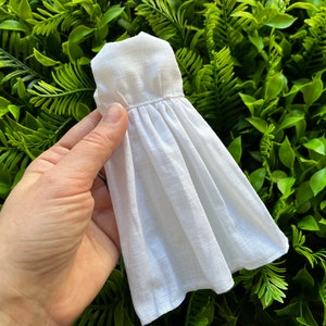 Peut inclure: Une robe en lin blanc avec une jupe plissée et un col simple.