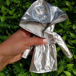 May include: A silver hooded jacket with a shiny metallic finish. The jacket has a zipper closure and long sleeves.