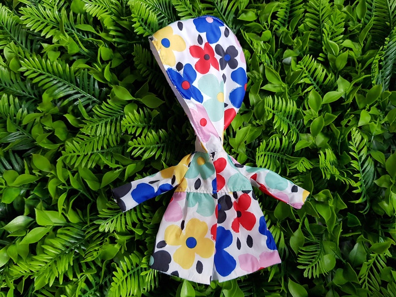 May include: A white raincoat with a hood, featuring a colorful floral pattern in shades of red, blue, yellow, and green.