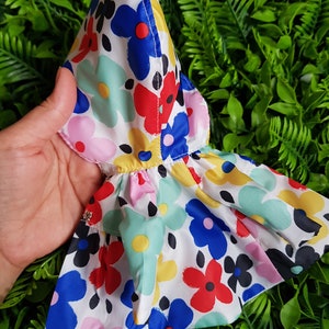 May include: A white hooded raincoat with a colorful floral print featuring red, blue, yellow, green, and pink flowers. The raincoat has a ruffled hem.