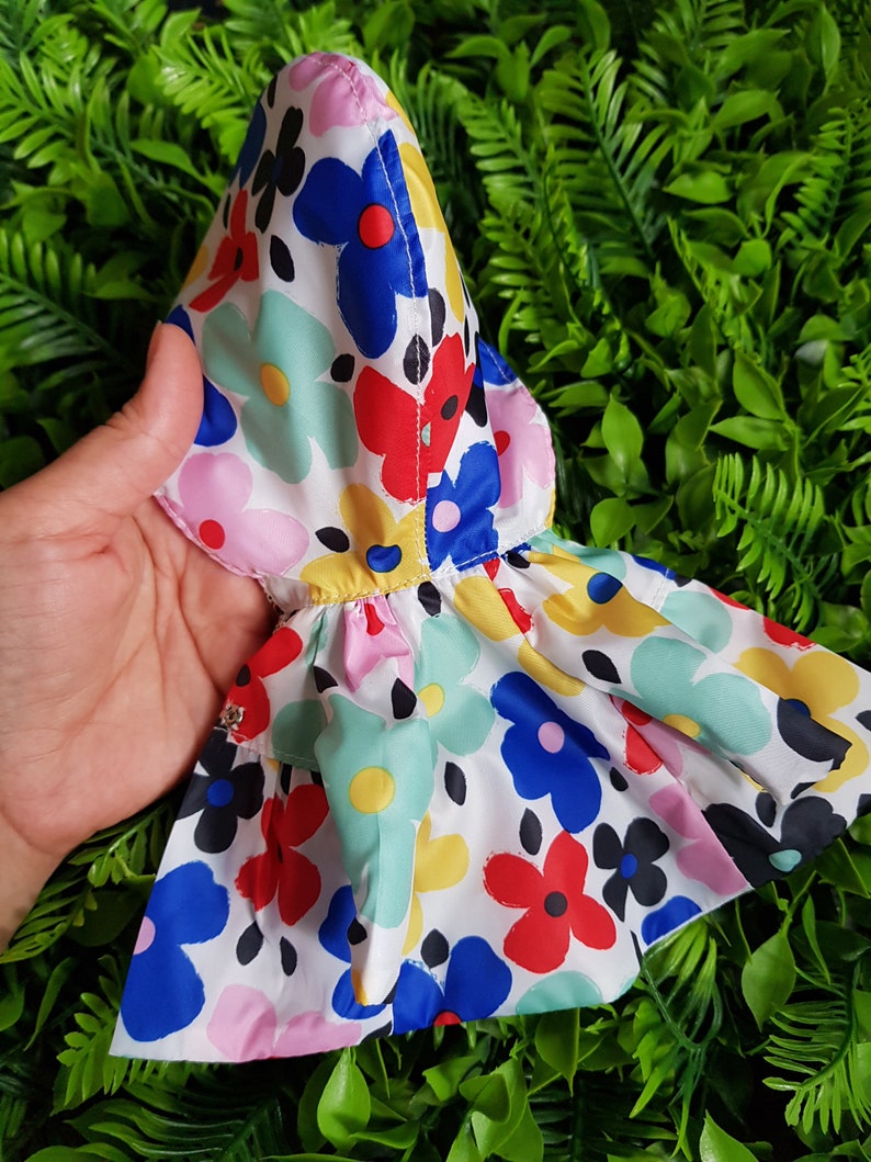 May include: A white hooded raincoat with a colorful floral print featuring red, blue, yellow, green, and pink flowers. The raincoat has a ruffled hem.