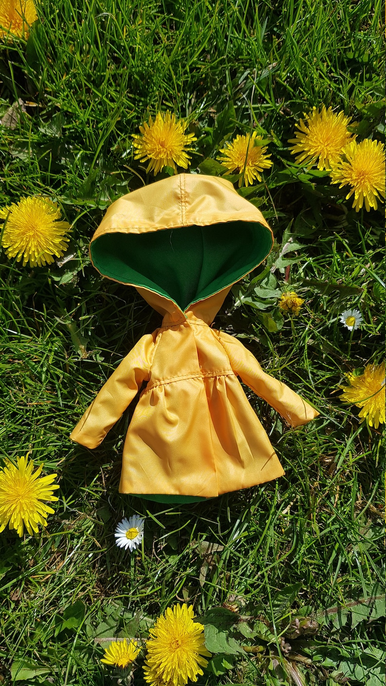 May include: A yellow raincoat with a green hood, lying on a bed of green grass with yellow dandelions.