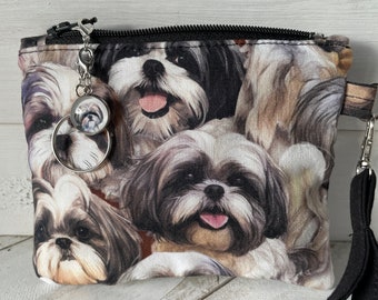 Könnte beinhalten: Eine schwarze Reißverschlusstasche mit einem schwarzen Riemen. Die Tasche ist aus Stoff und hat einen Druck mit mehreren Shih Tzu Hunden. Ein silberner Anhänger mit einem Shih Tzu Bild ist am Reißverschluss befestigt.