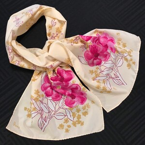 May include: A cream-colored silk scarf with a floral print. The flowers are pink and yellow and have a vintage look. The scarf has a small label that says "Unao".