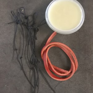 Puede incluir: Vista a&eacute;rea de una colecci&oacute;n de art&iacute;culos. Un peque&ntilde;o recipiente de pl&aacute;stico transparente contiene una sustancia de color amarillo claro. Un trozo de cord&oacute;n de cuero rojo est&aacute; enrollado. Tambi&eacute;n hay una longitud de cuerda negra anudada.
