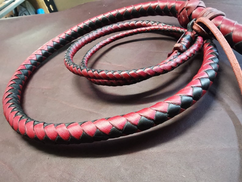 May include: A braided leather whip with a red and black pattern. The whip is coiled and ready for use.