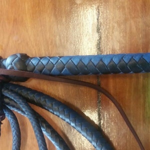 Puede incluir: Un l&aacute;tigo de cuero negro y azul con un mango trenzado y un cuerpo trenzado. El l&aacute;tigo est&aacute; hecho de cuero y tiene una correa de cuero marr&oacute;n. El l&aacute;tigo est&aacute; sobre una superficie de madera.