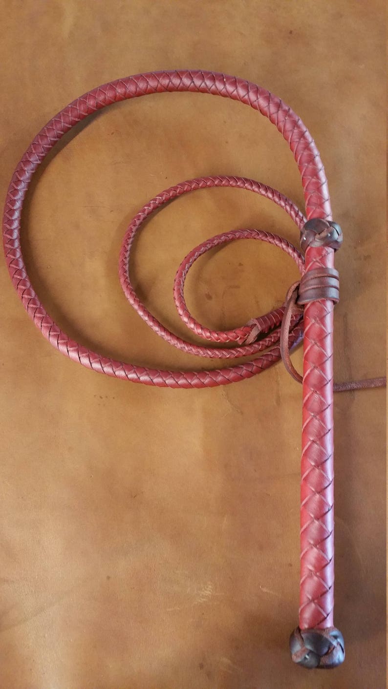 May include: A red leather bullwhip with a braided handle and a long, braided lash. The whip is coiled in a circle.