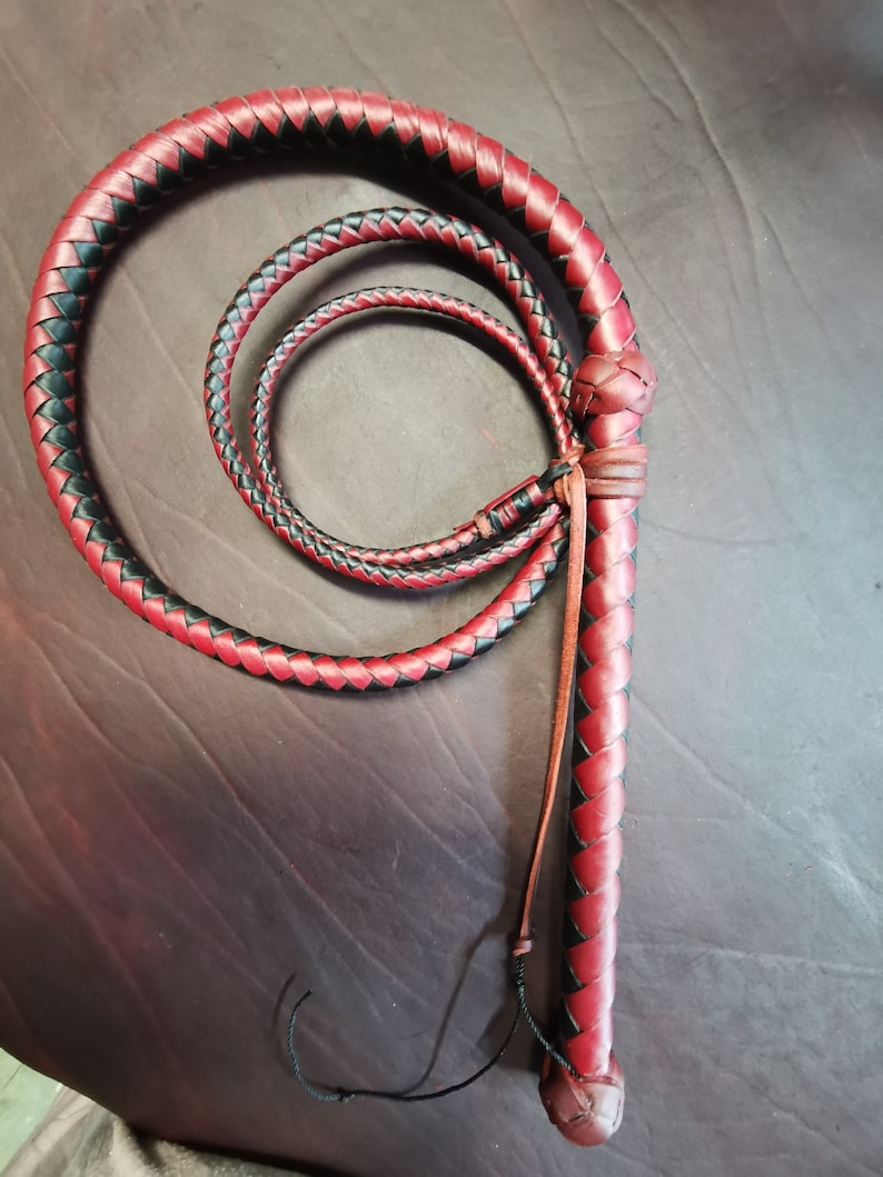 May include: A red and black leather bullwhip with a braided handle. The whip is coiled and ready to be used.