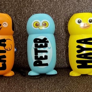 May include: Three colorful, cartoon-like figures. The first is orange with the name "LAYA" in black. The second is blue with the name "PETER" in black. The third is yellow with the name "MAYA" in black. Each figure has a unique animal-like design.