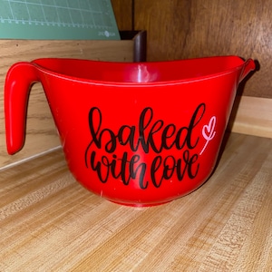 May include: Red plastic mixing bowl with a black vinyl decal that says "baked with love" and a small pink heart.