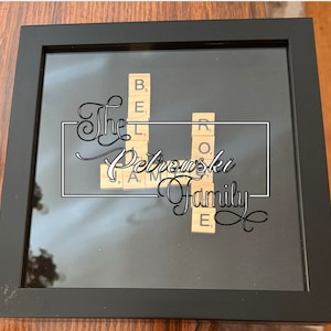 May include: A black framed shadow box with a white background. The words "The Petrowski Family" are written in cursive script. The words are spelled out using letter tiles from a Scrabble game.