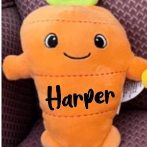 May include: Orange plush carrot toy with a smiling face, black eyes, and green leafy top. The name "Harper" is stitched in black across the front. The toy has small arms and feet.