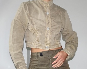 May include: A cropped beige denim jacket with a stand-up collar and button closure. The jacket has a slightly distressed look and features decorative stitching on the front and back.